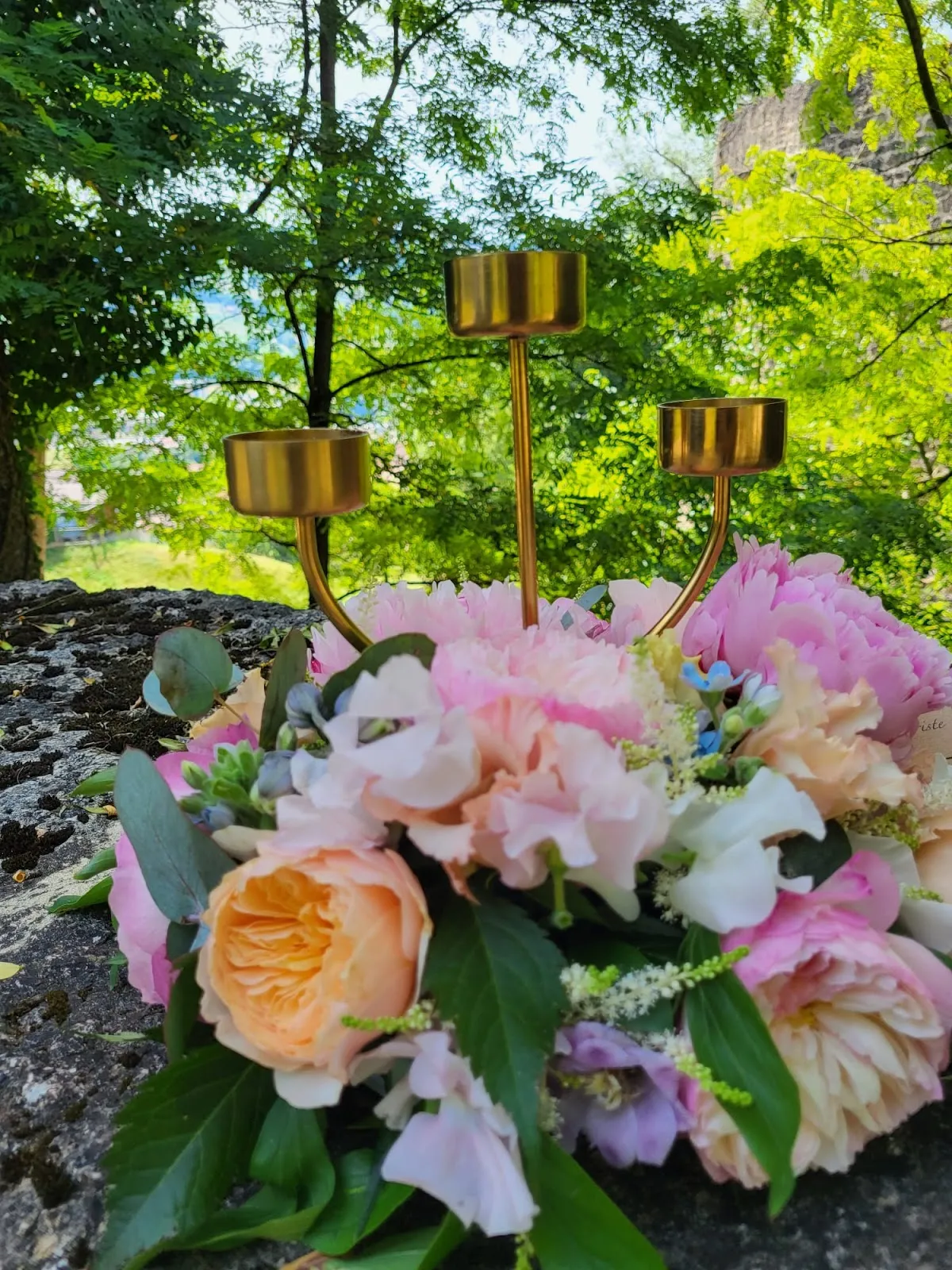 Bouquet aux tons pastel : pivoines roses, roses pêche et verdure, sur une pierre au jardin
