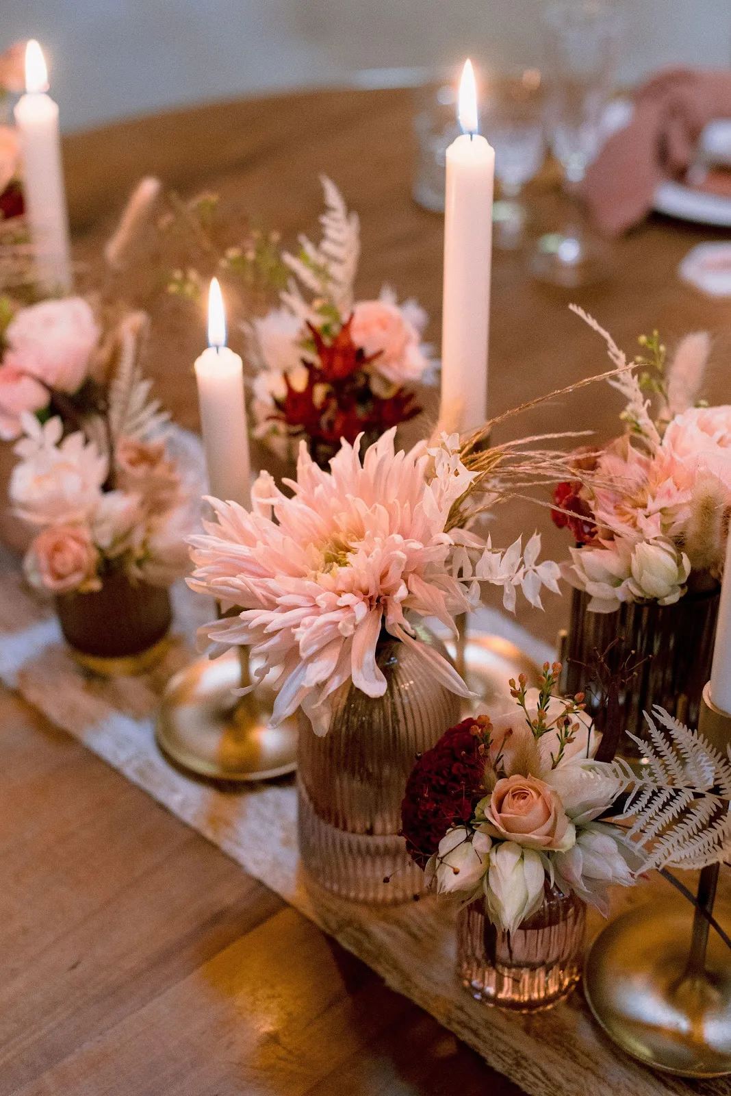 Centres de table : dahlias roses et bougies dans des vases dorés sur une table en bois
