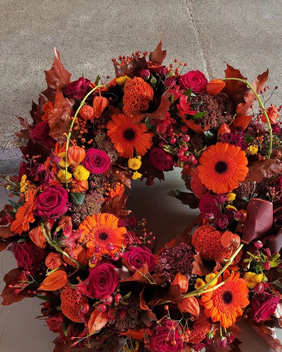 Couronne de fleurs aux tons d’automne : gerberas orange, roses rouges et feuillage cuivré